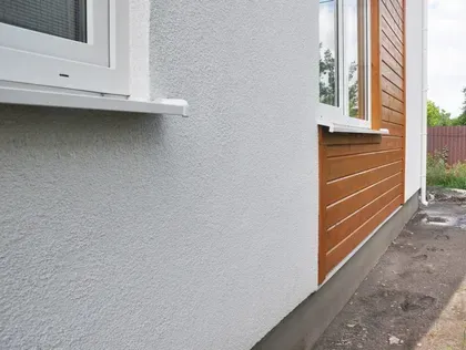 Exterior house wall with white window trim and orange siding beside a narrow paved path
