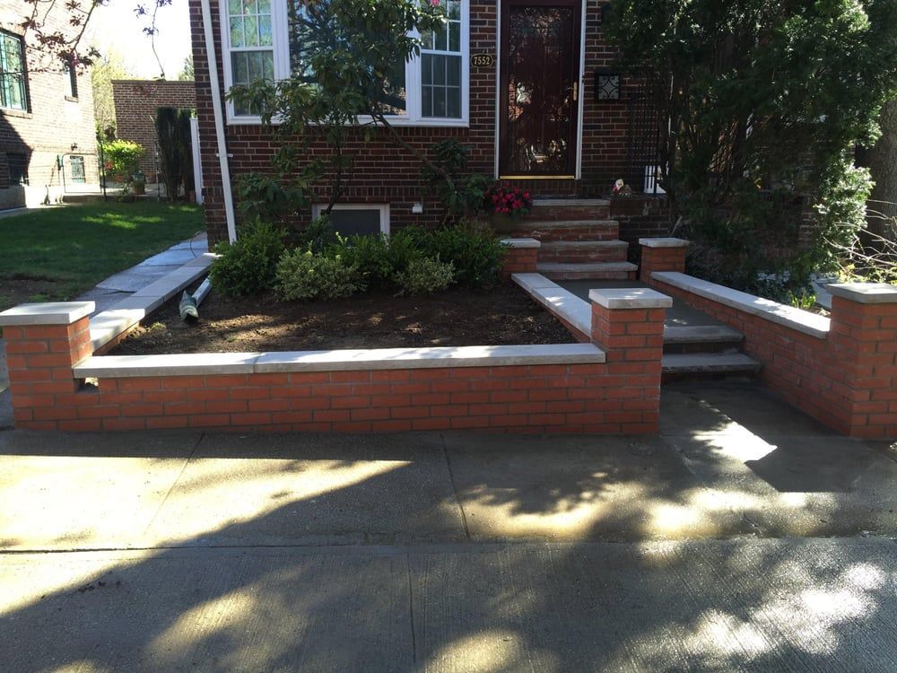 Brick house front yard with low brick retaining walls, steps, and shrubs in sunlight