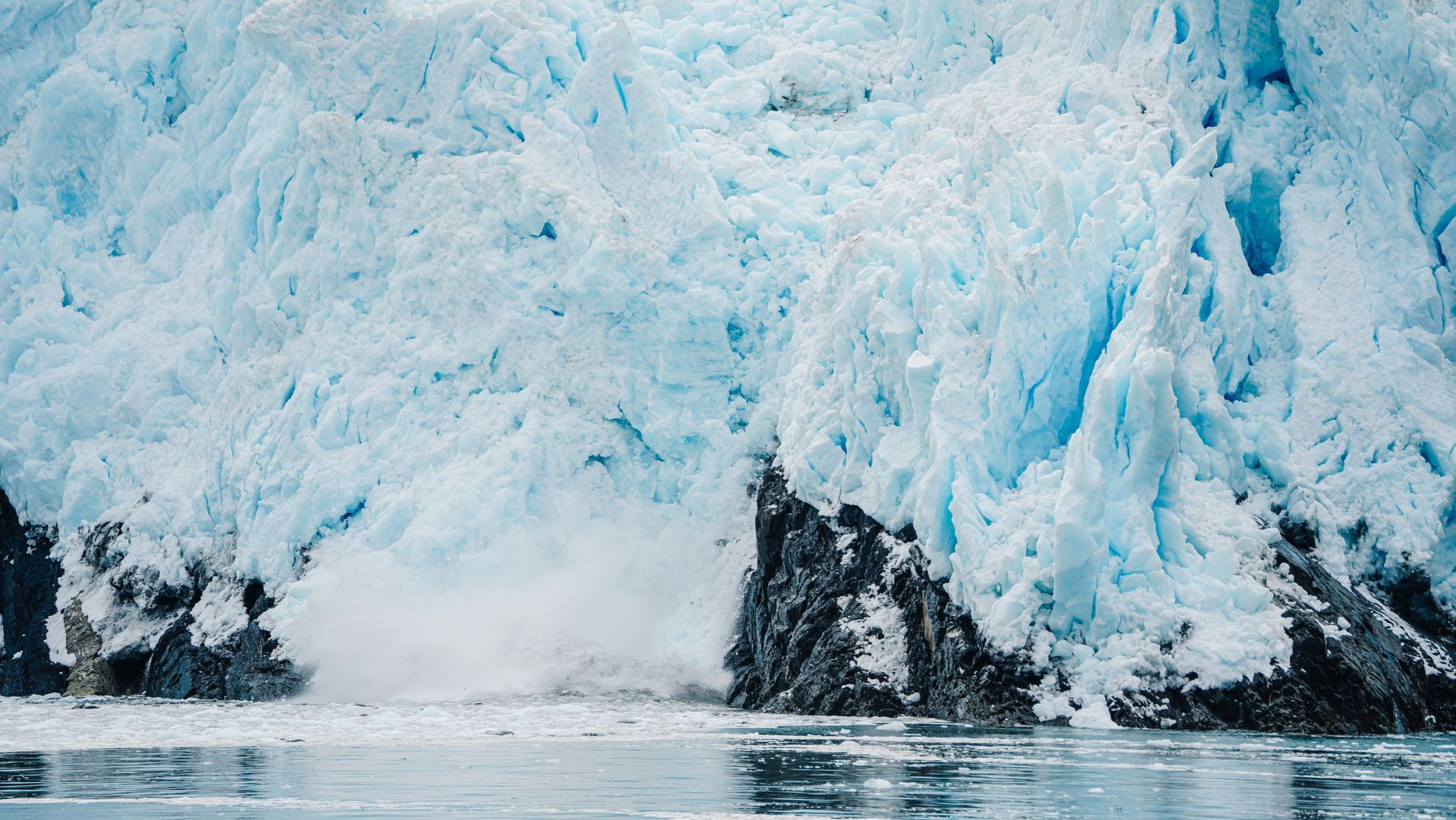 Blue glacier melting into dark seawater with icy cliffs and floating ice chunks