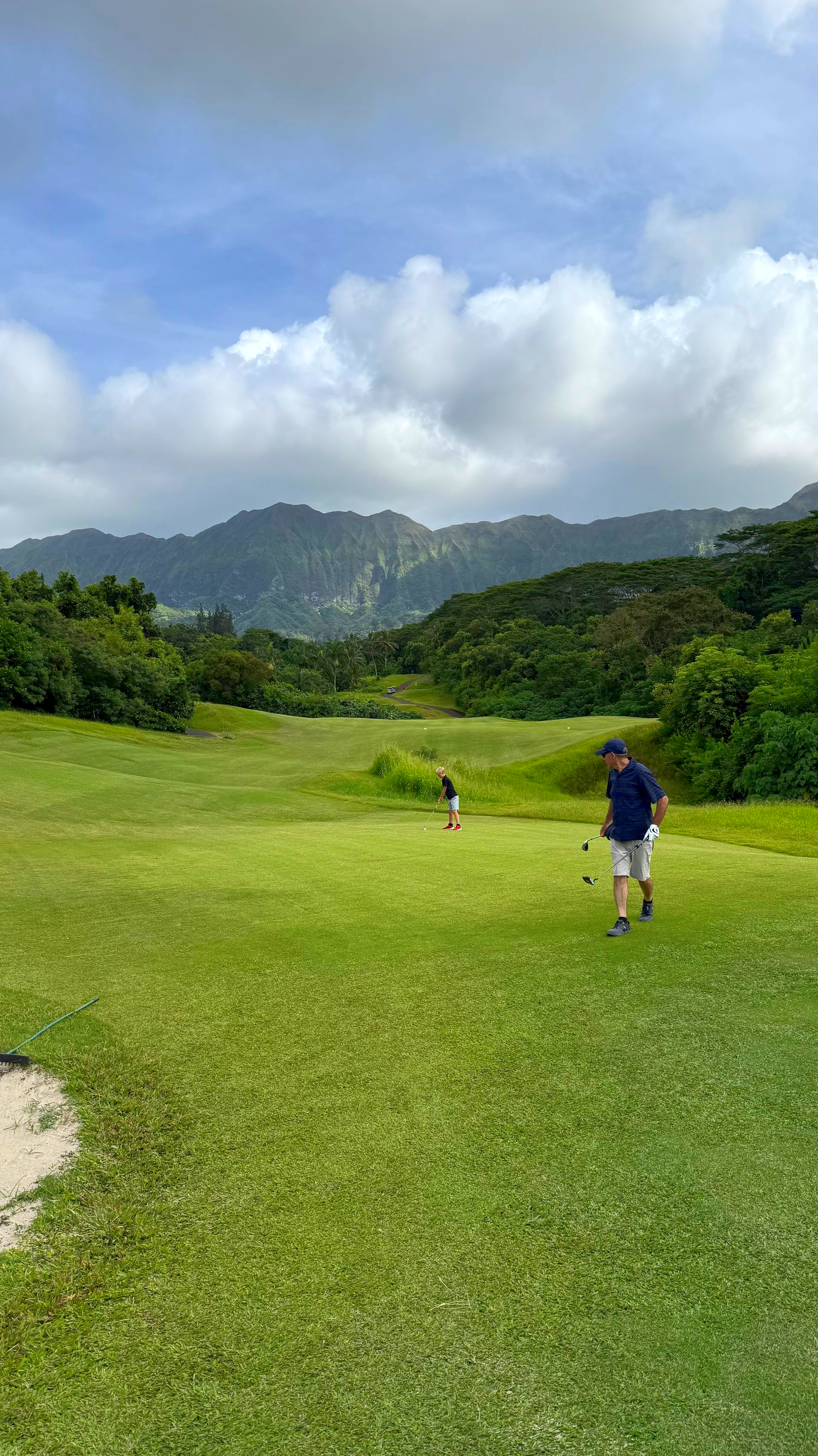 Golfers on a green fairway with mountains and cloudy sky in the background