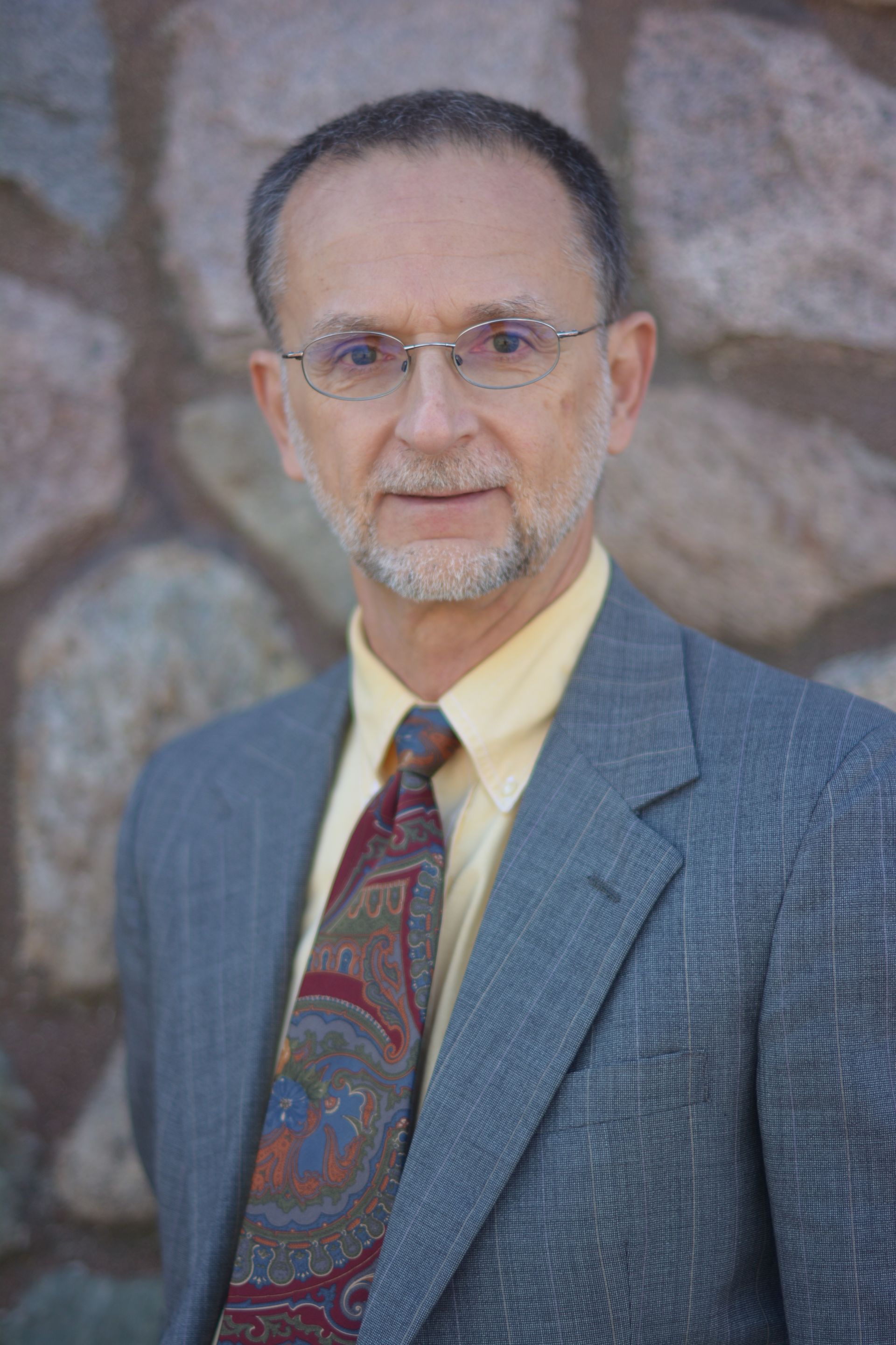 A man in a suit and tie is standing in front of a bookshelf.