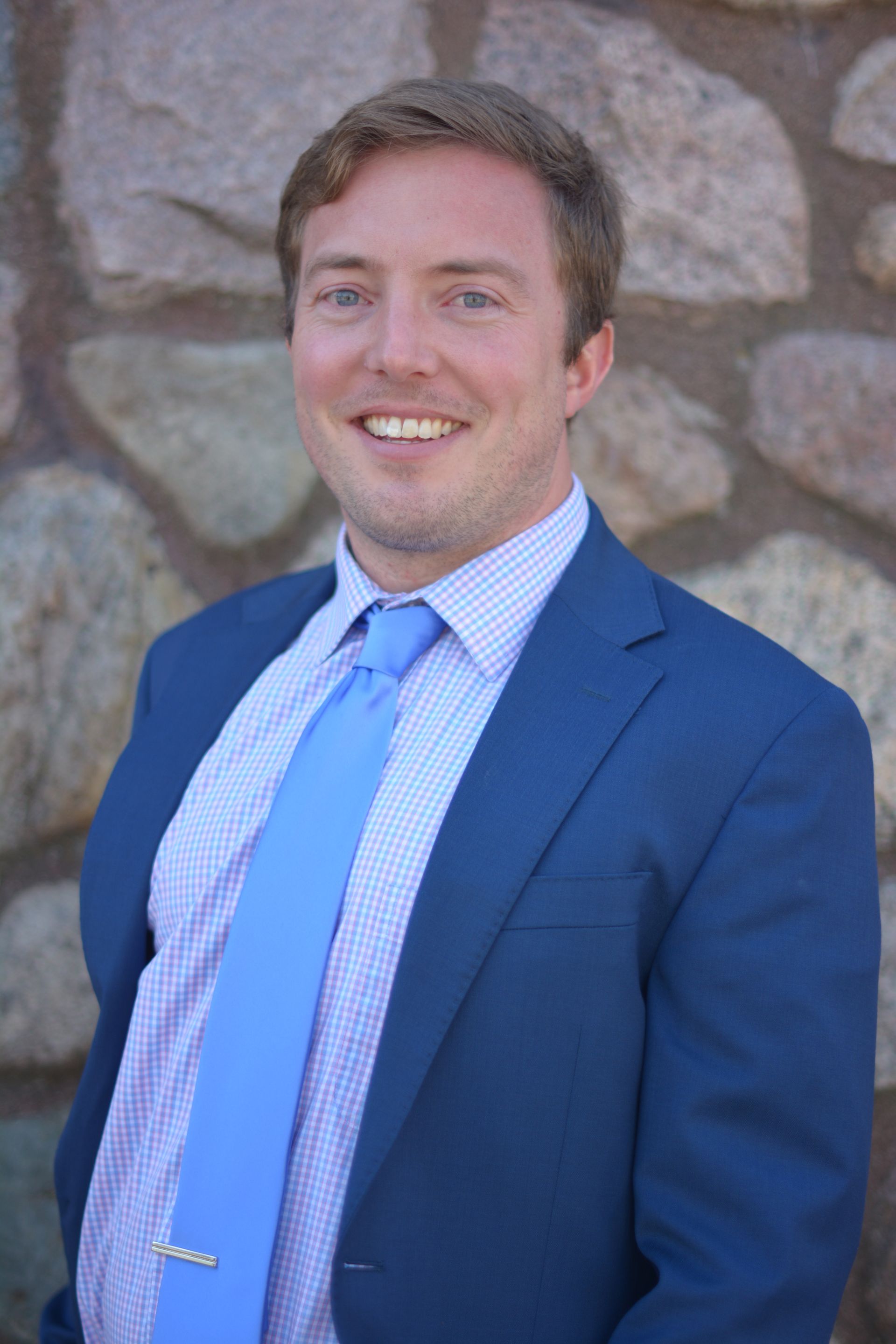 A man in a suit and tie is standing in front of a bookshelf.