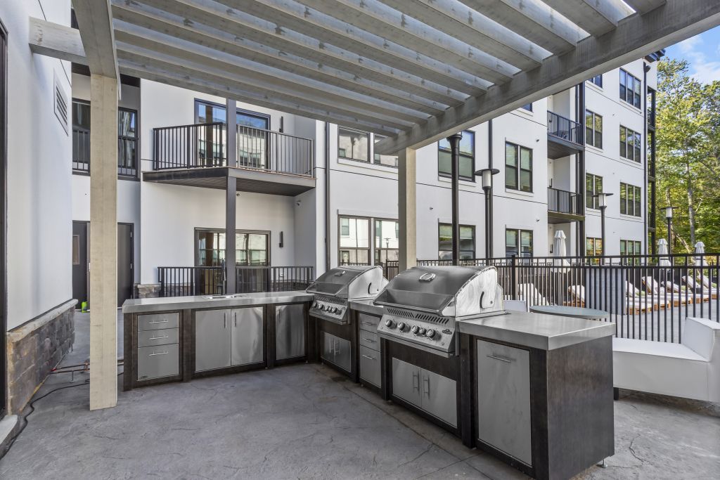 Covered outdoor communal grill area with stainless steel counters and grills in a modern apartment courtyard
