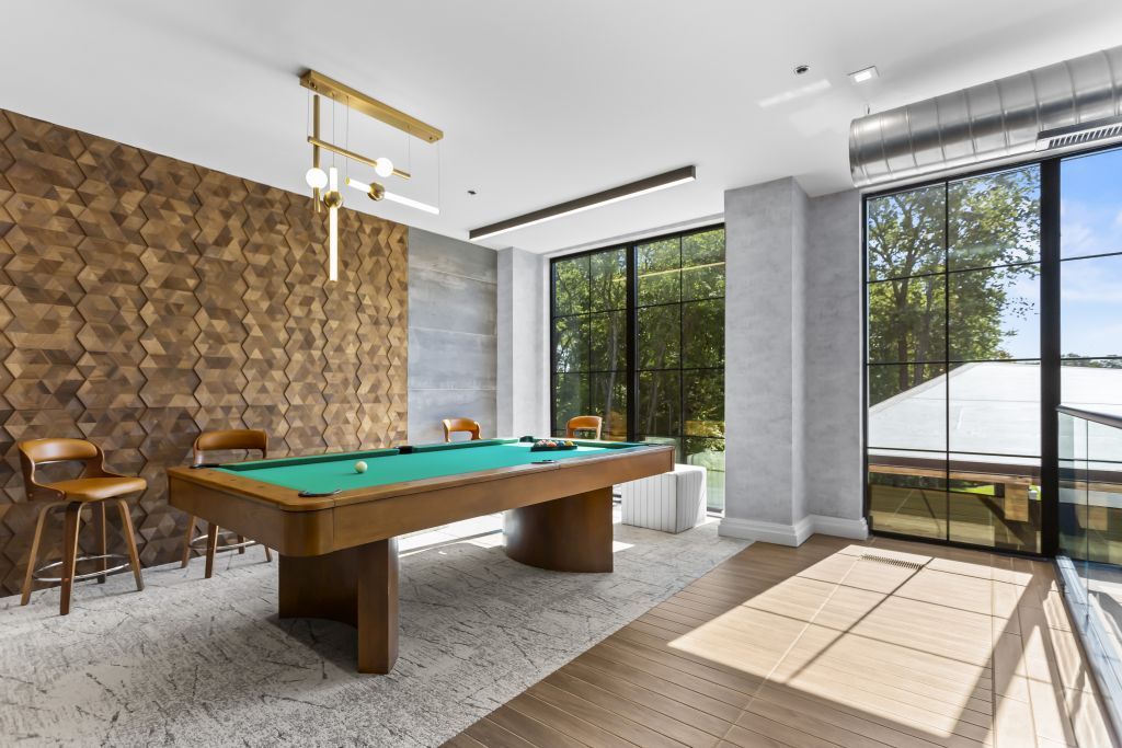 Modern game room with pool table, wood accent wall, and floor-to-ceiling windows looking outside