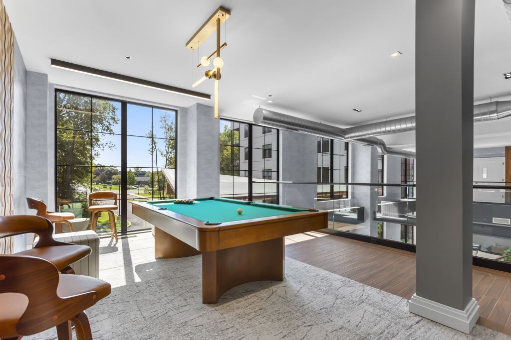 Bright game room with pool table, modern seating, and large windows overlooking greenery