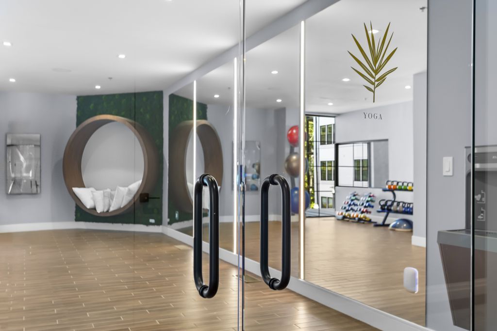 Modern lobby with glass doors, wood floor, large round mirror, and seating area
