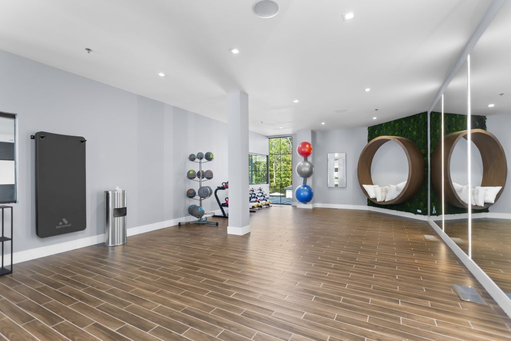 Bright fitness studio with hardwood floors, wall mirrors, exercise balls, and weights by a large window