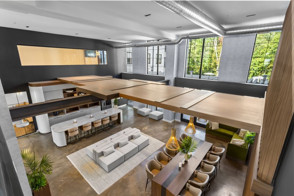 Modern open-concept office lounge with wooden tables, white seating, and large windows overlooking greenery