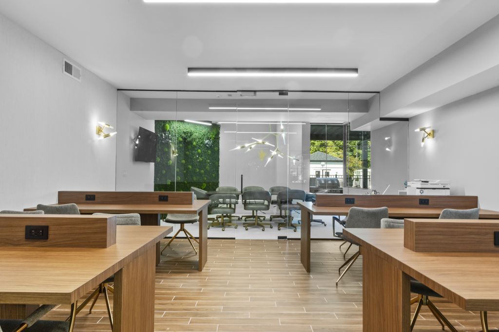 Modern classroom with wooden desks, white walls, and large windows opening to a green outdoor view