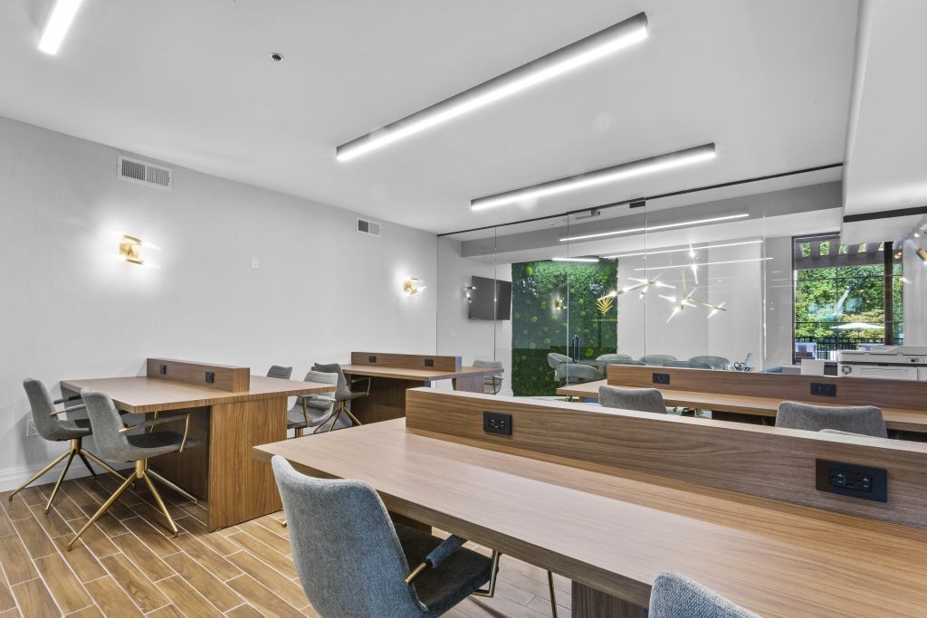 Modern open office with long desks, chairs, and bright windows overlooking greenery