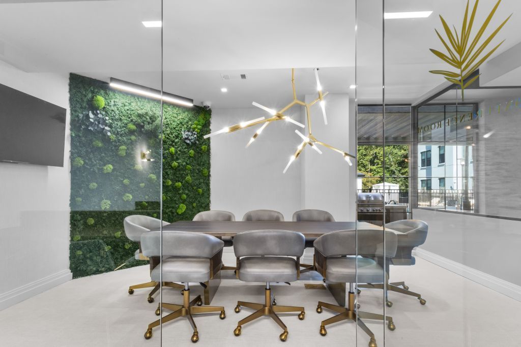 Modern conference room with glass walls, gray chairs, a long table, and a green plant wall