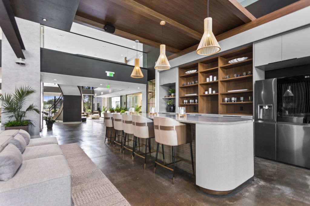 Modern open-plan kitchen and living area with wood beams, bar stools, pendant lights, and a large island.
