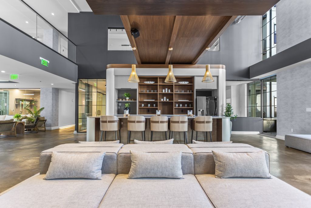 Modern hotel lobby with a central bar, tall windows, pendant lights, and a beige sofa in the foreground