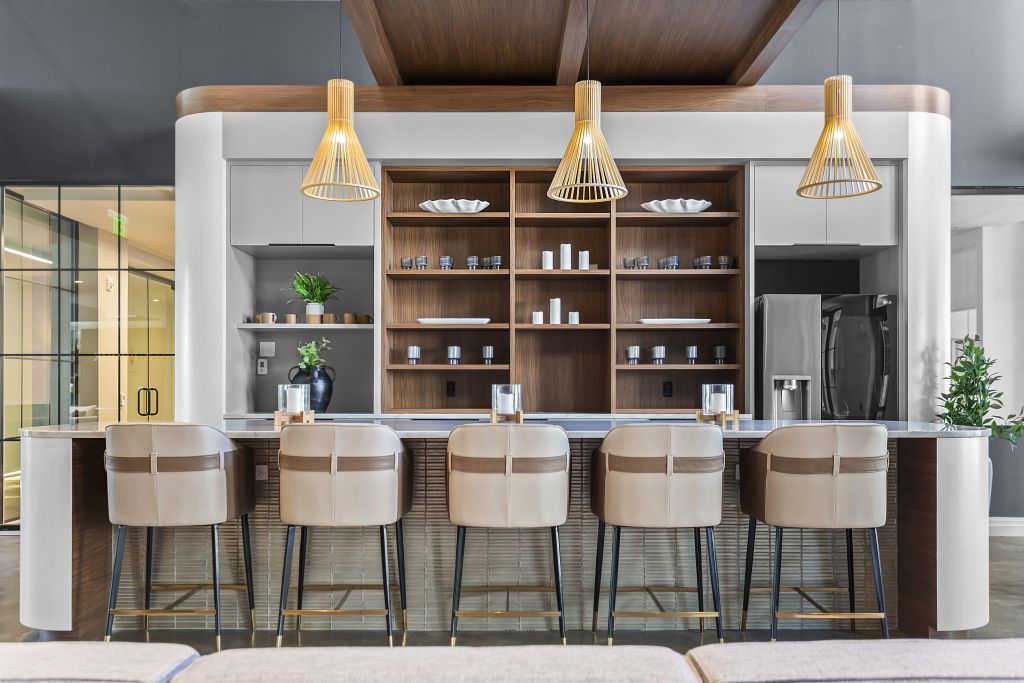 Modern kitchen bar with five stools, pendant lights, wooden shelves, and a polished island counter