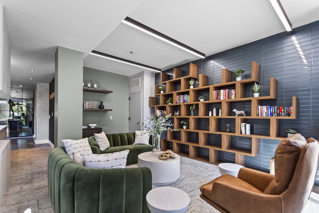 Modern living room with green sofa, tan chair, and wooden wall-mounted shelving
