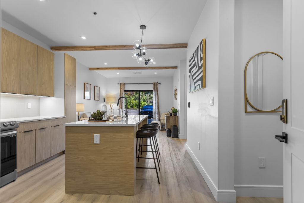 Bright modern kitchen with wood island, white cabinets, bar stools, and a view to a patio door.