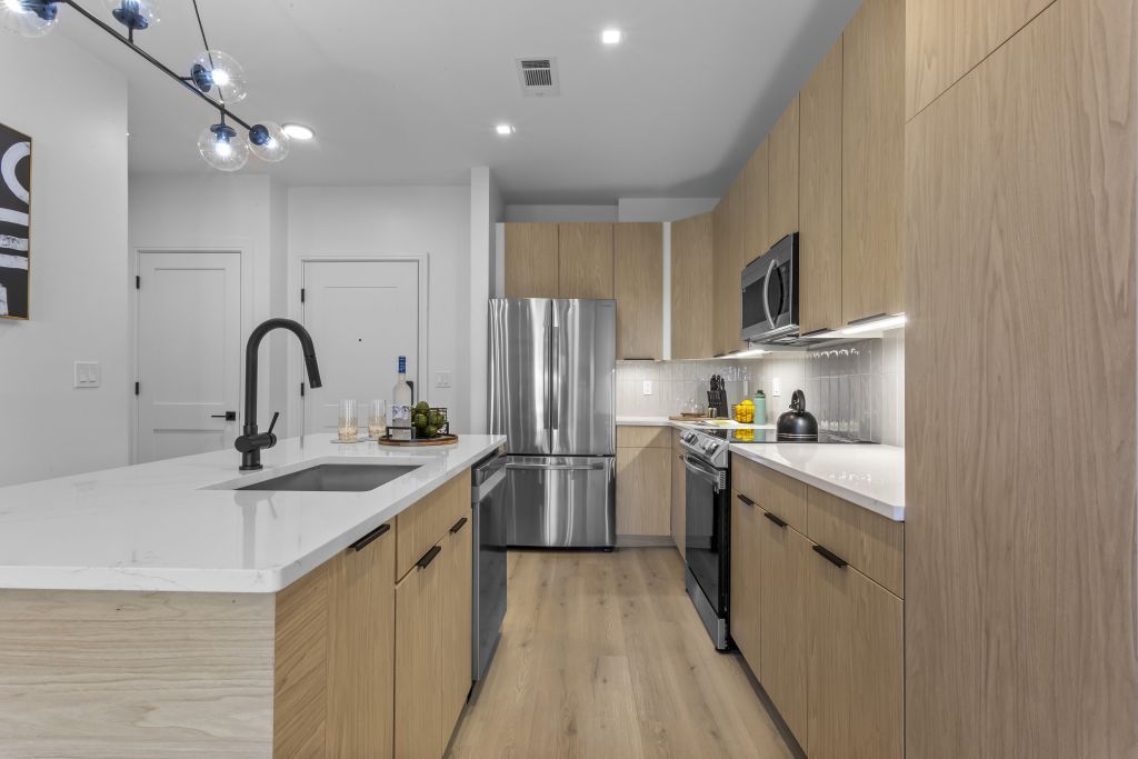 Modern kitchen with white island, black faucet, stainless steel appliances, and light wood cabinets