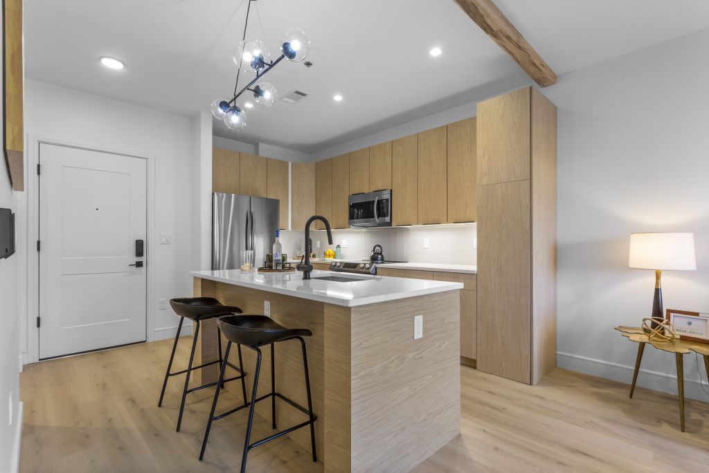 Modern kitchen with island, wood cabinets, stainless appliances, and two bar stools in an open living space
