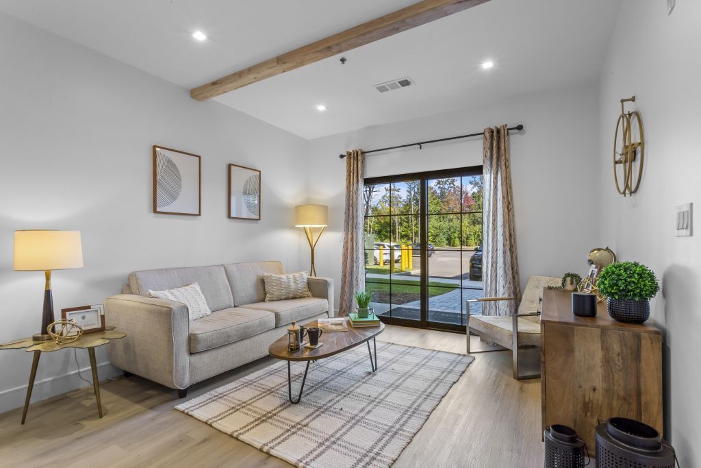 Bright living room with white sofa, wooden coffee table, lamp, rug, and sliding doors to a patio.