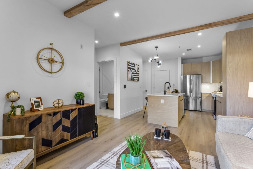 Bright open living room with wood beams, console table, sofa, and kitchen in the background