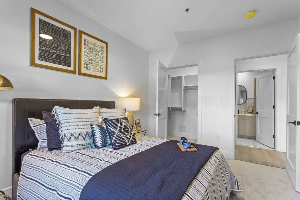 Neatly made bedroom with patterned bedding, dark blue throw, and a closet and vanity in the background