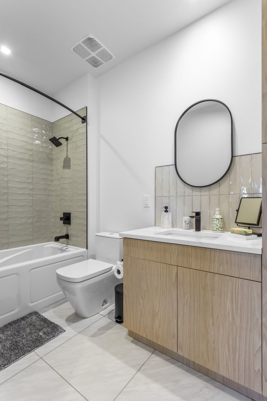 Modern bathroom with glass shower, toilet, and wood vanity beneath an oval mirror.