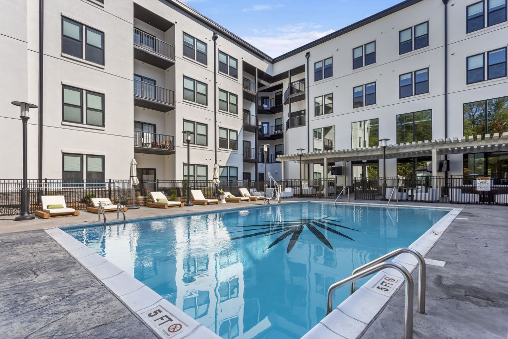 Apartment courtyard pool with blue water, lounge chairs, and surrounding modern buildings