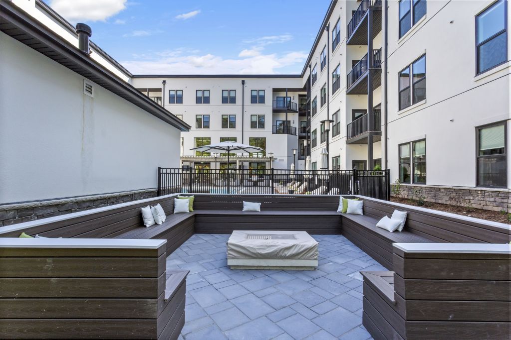 Modern apartment courtyard with wooden benches, a central fire pit, and surrounding white buildings.