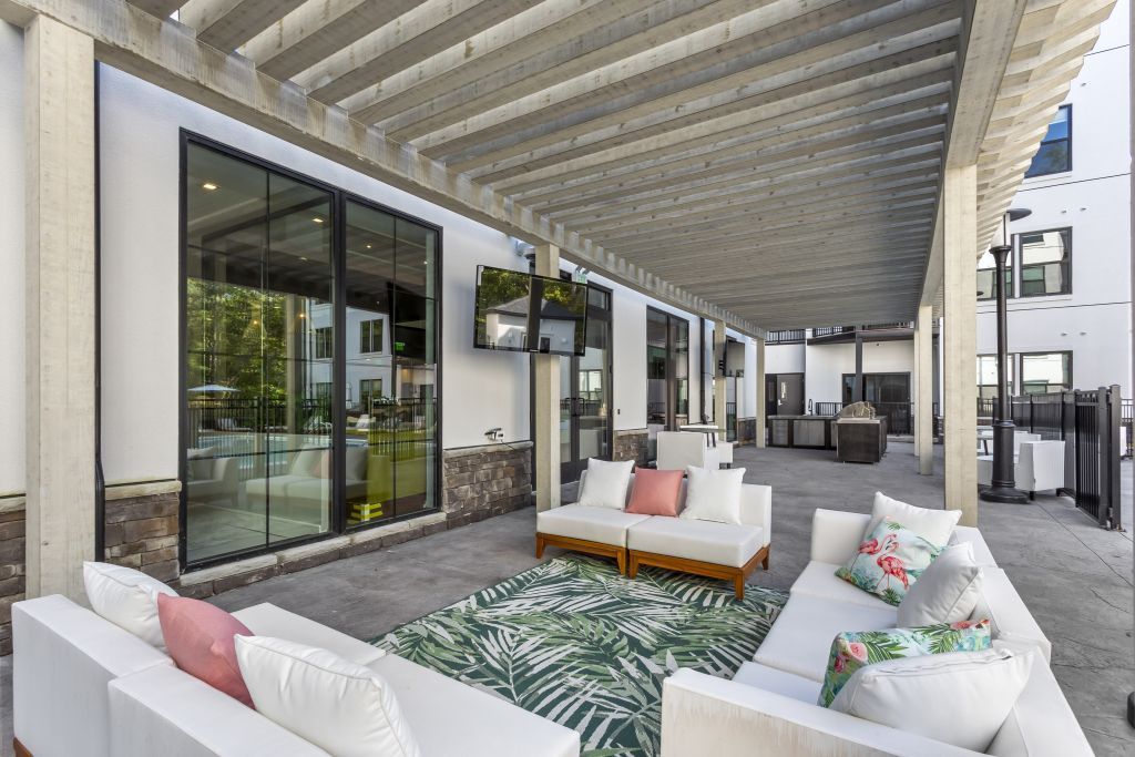 Covered patio lounge with white sofas, patterned rug, and large sliding glass doors