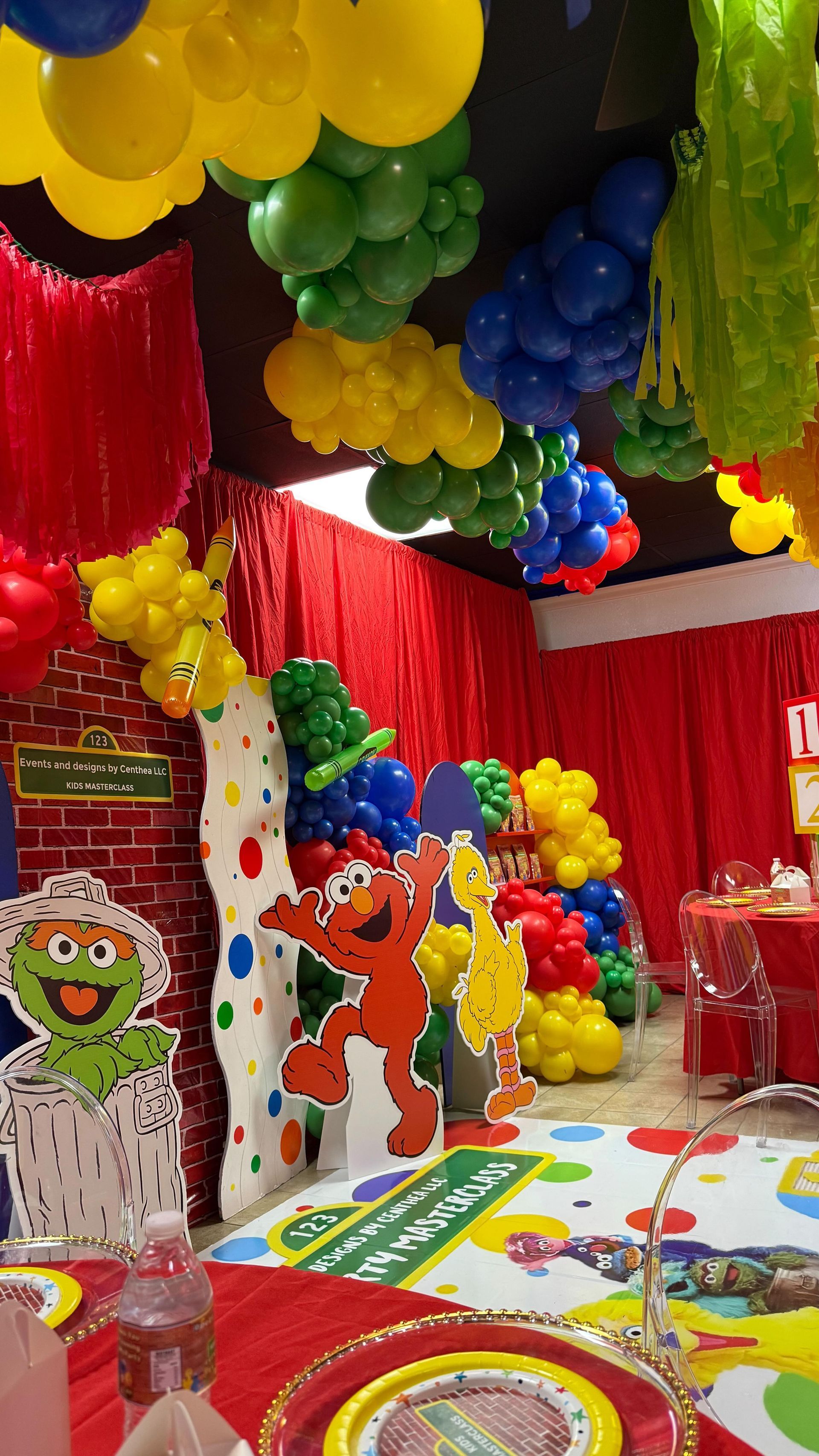 Balloon-filled party display with colorful clown cutouts, red curtains, and a decorated floor
