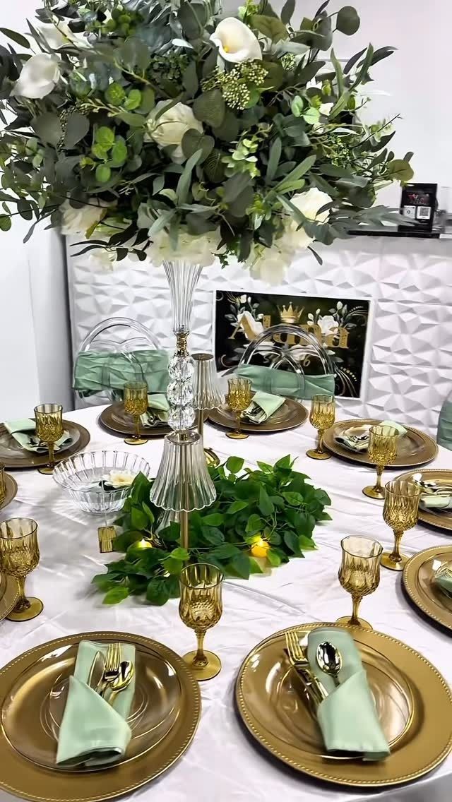 Elegant gold-and-white table setting with floral centerpiece and framed decor at a reception table