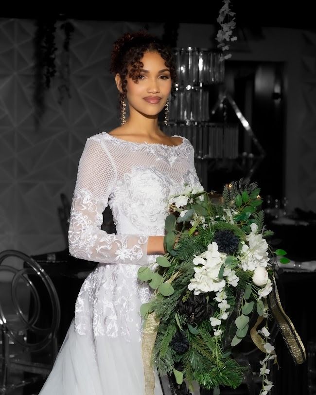 Woman in a white lace dress holding a cascading green and white bouquet in a dimly lit venue