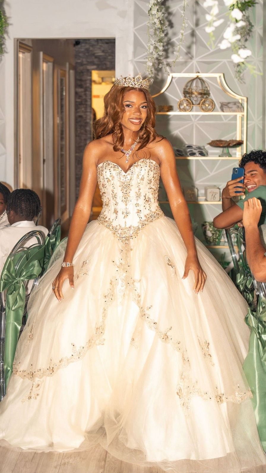 Woman in a cream, sparkling ball gown standing at a decorated indoor event venue