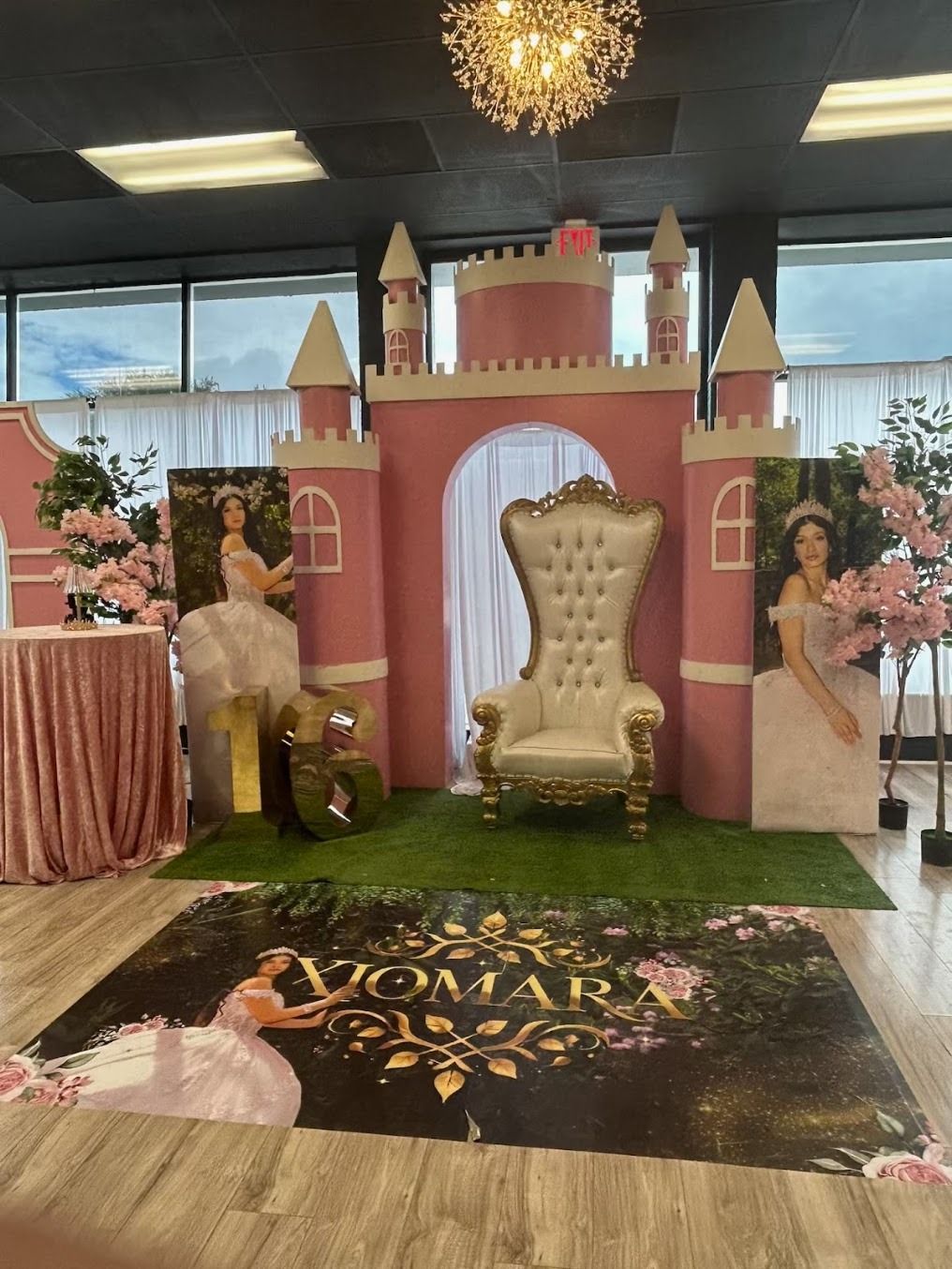 Pink castle-themed event stage with gold throne chair, floral decor, and a birthday floor sign