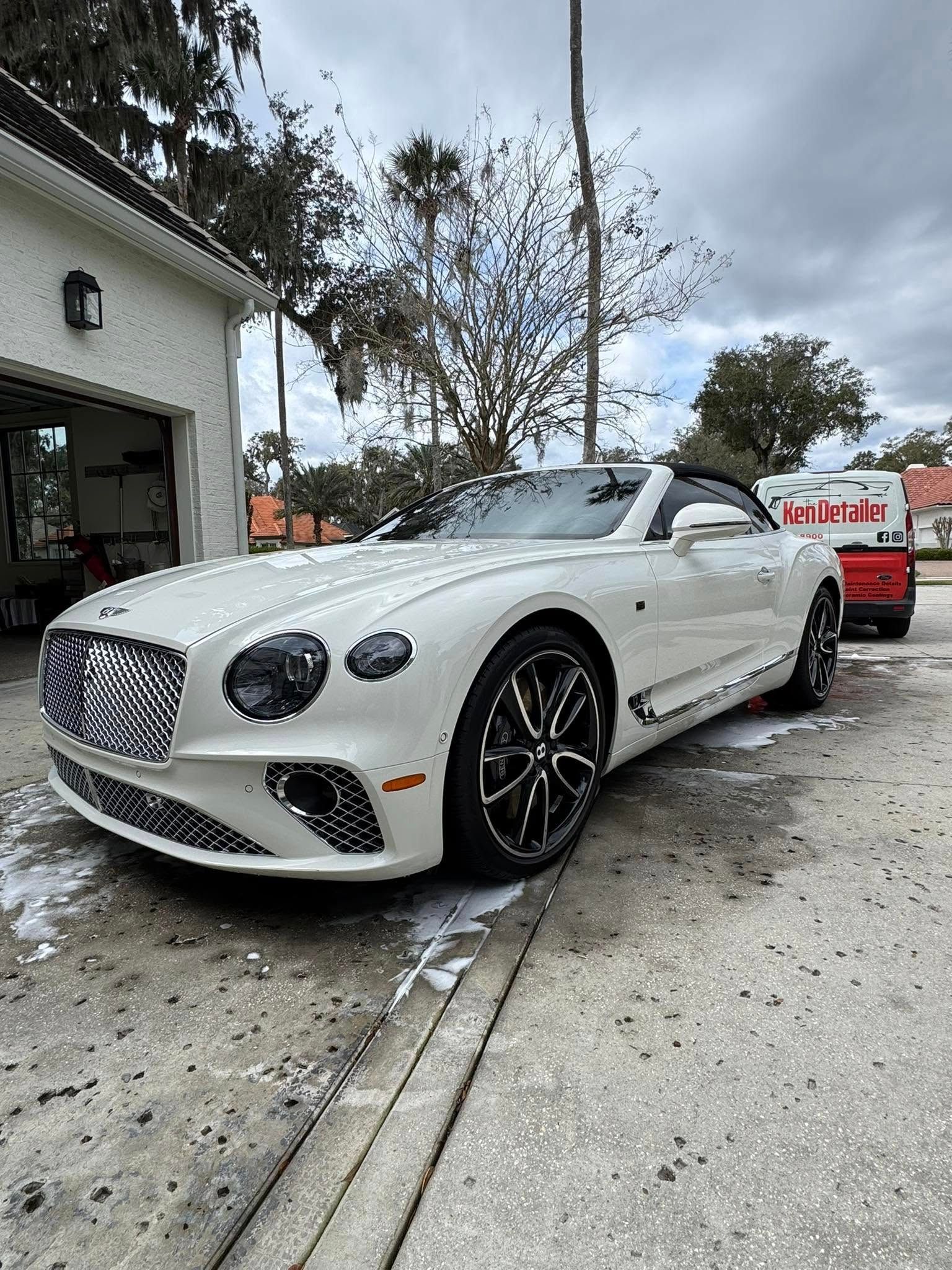 White Bentley convertible being washed in front of a building.