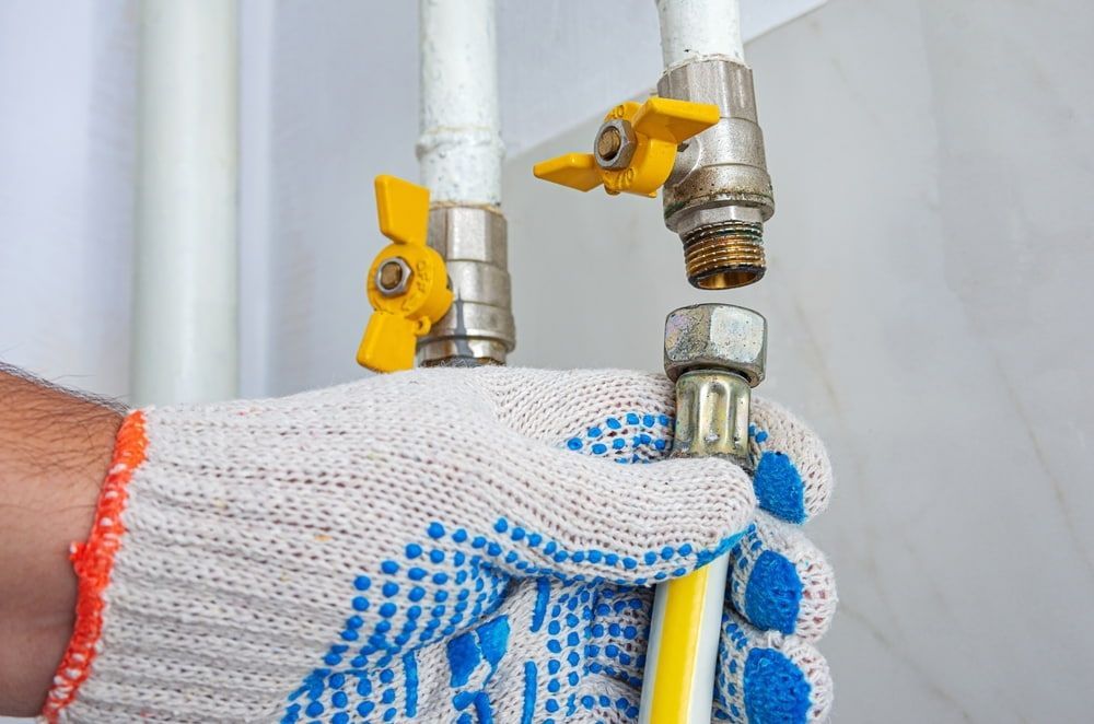 A Person Is Fixing A Gas Pipe With A Yellow Valve — Aquafix Plumbing Services in Bowral, NSW