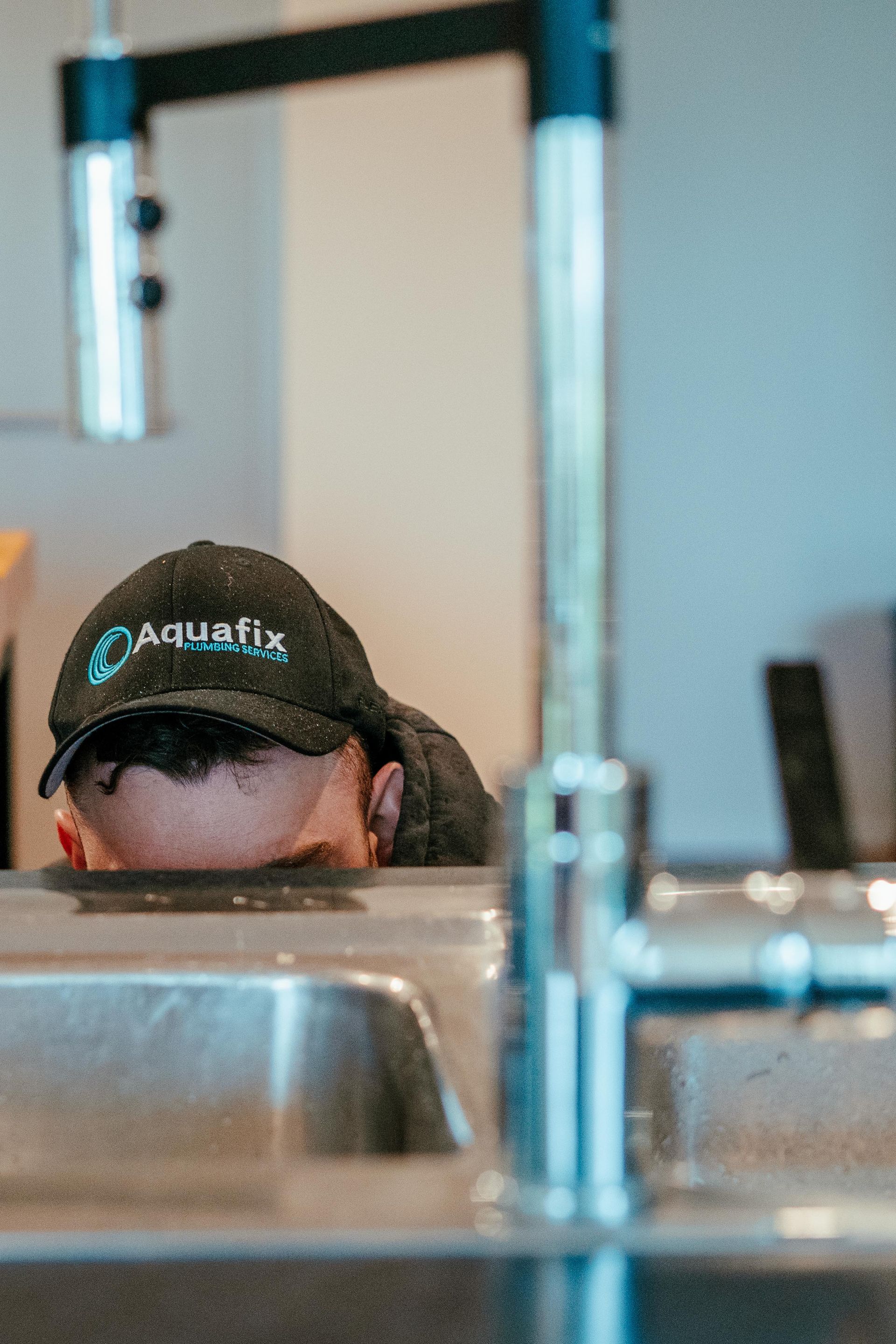 Person wearing a cap peeks over a stainless steel counter in a kitchen or café setting. — Aquafix Plumbing Services in Bowral, NSW