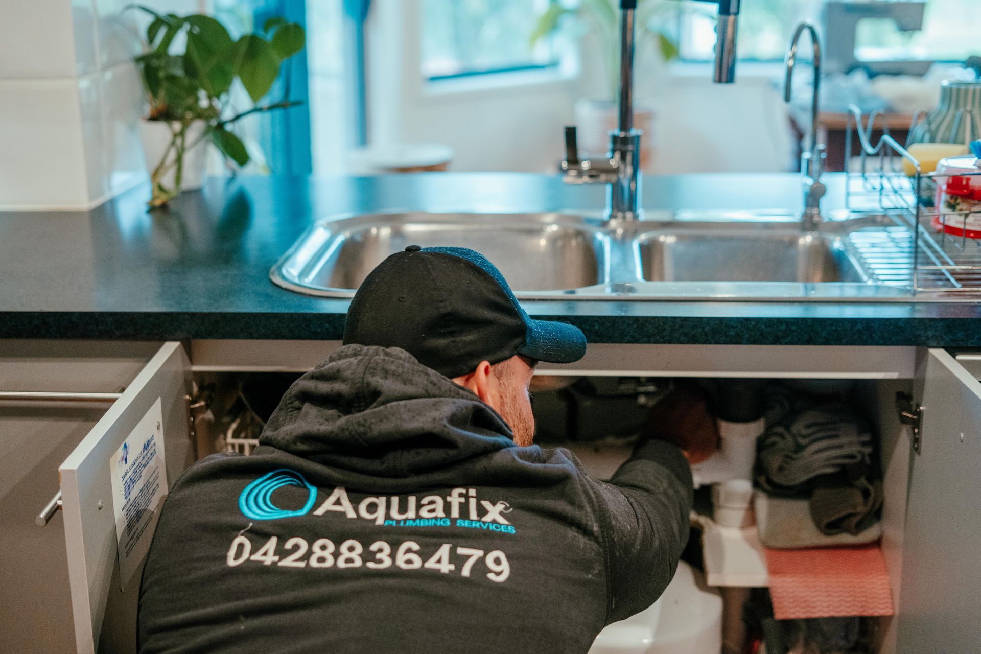 Plumber working under a kitchen sink, repairing plumbing in a bright kitchen.