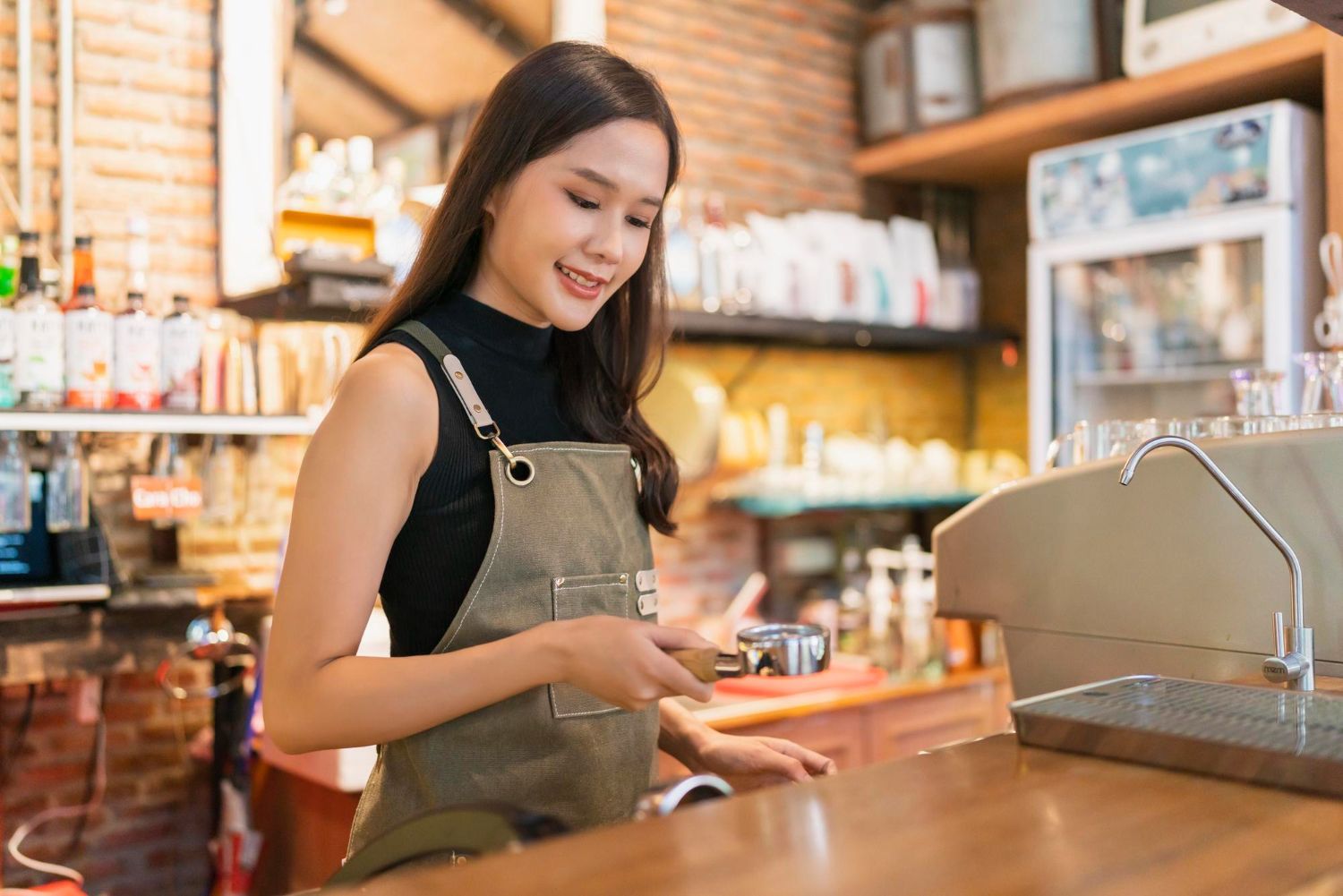 Barista in an apron, making coffee at a counter with equipment and supplies visible in the cafe.