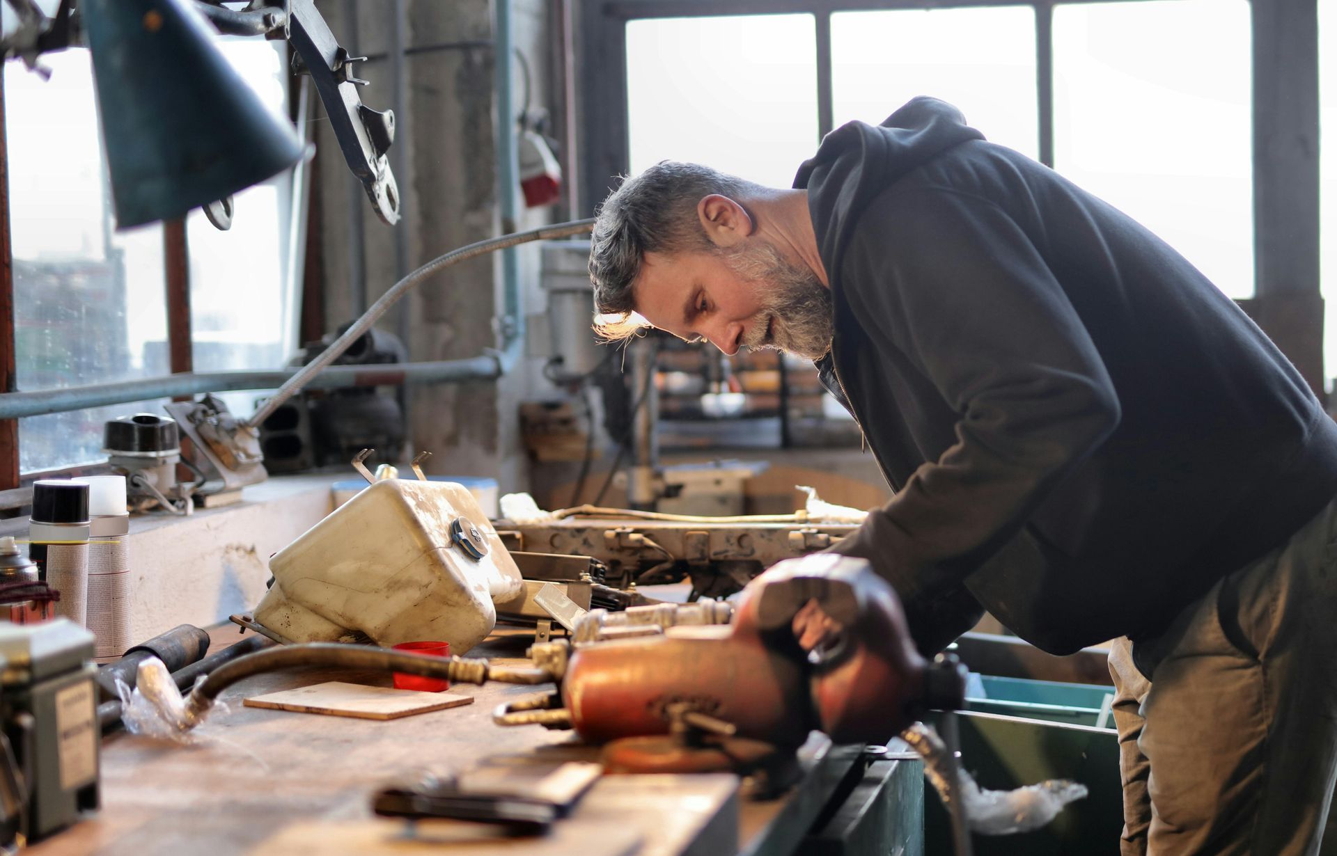 Man in workshop leans over workbench, working on mechanical parts.