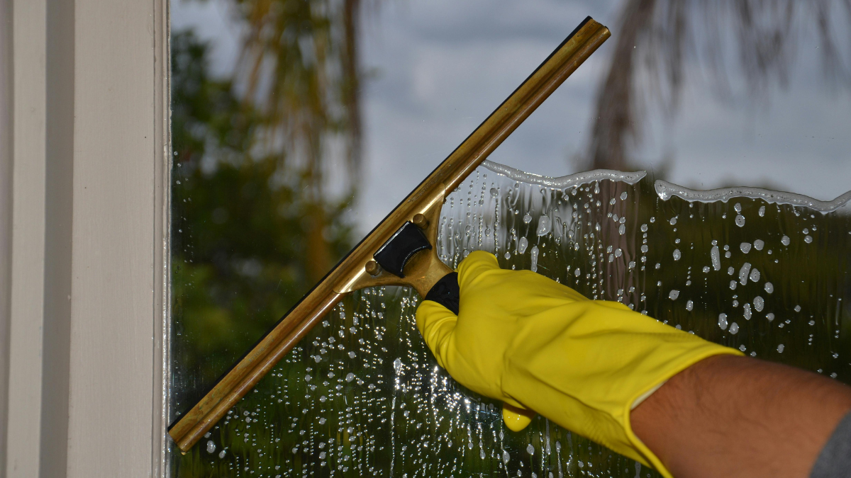 A person in yellow gloves using a squeegee to clean a window.