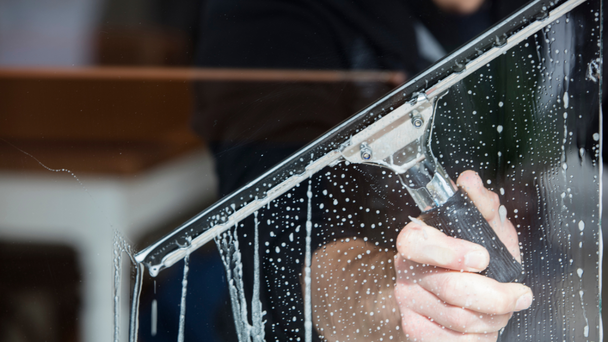 Person squeegeeing a window, soapy water visible.