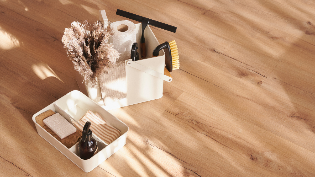 Cleaning supplies in white containers on a light wood floor with sunlight.