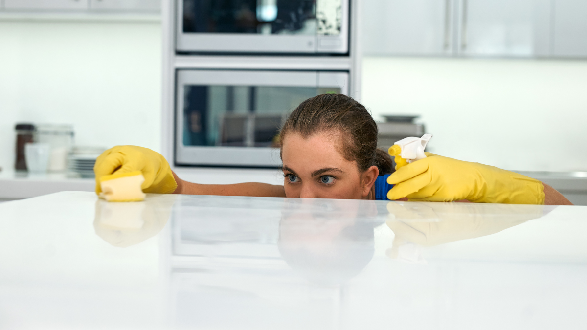 A person wearing yellow rubber gloves cleaning a white countertop in a kitchen.