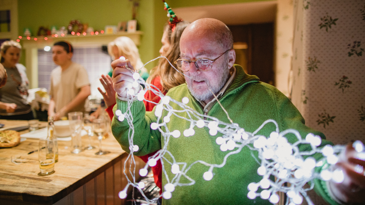 A man in a green sweater is holding a string of Christmas lights.