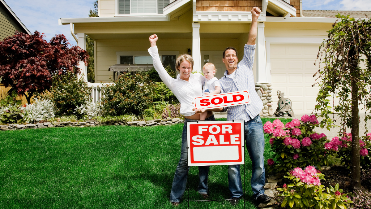 A family is standing in front of a house holding sold signs.