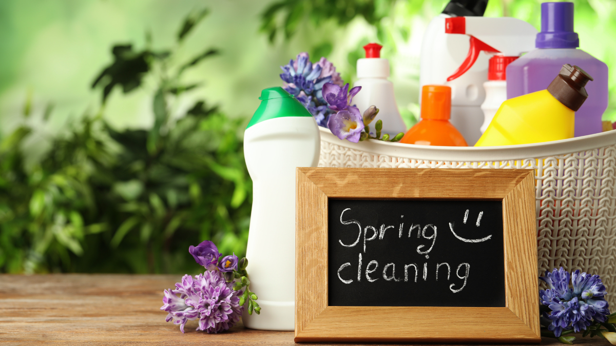 Spring cleaning supplies in a wooden box with a chalkboard sign and purple flowers