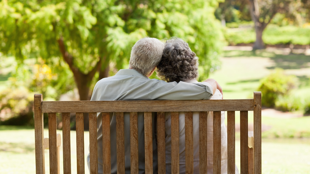 An elderly couple is sitting on a wooden bench in a park.