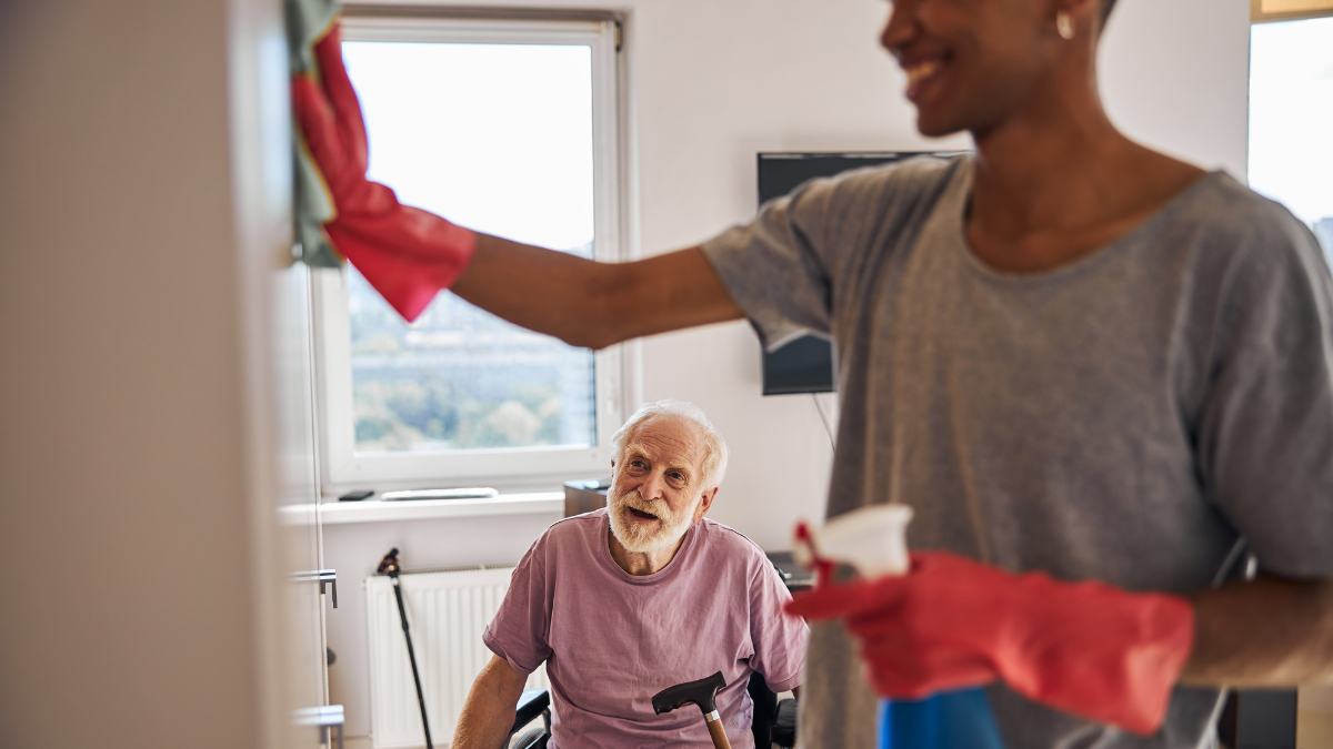 An elderly man in a wheelchair is sitting next to a man cleaning a window.