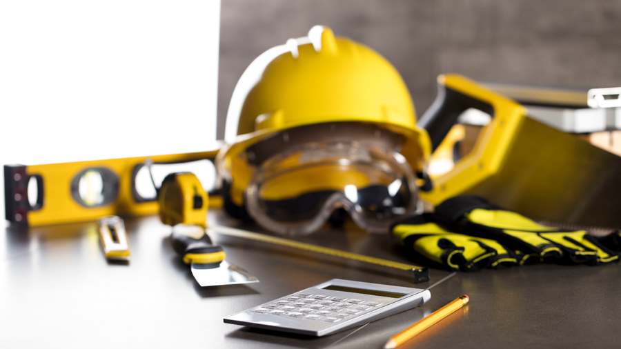 Yellow hard hat, safety goggles, gloves, tape measure, and calculator on a workbench